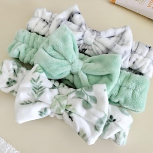 May include: Three plush headbands with bows. One headband is white with green leaves, one is green, and one is white with a marble pattern.