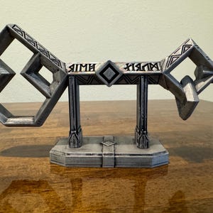 May include: A silver-colored key with intricate details and a diamond-shaped center piece. The key is on a stand with the words "AIMH" and "XIAM" inscribed on the sides.