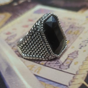 May include: A silver ring with a large black gemstone. The ring has a textured band.