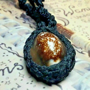 May include: A brown and white seashell pendant with black braided cord. The cord is knotted around the shell and forms a loop at the top.