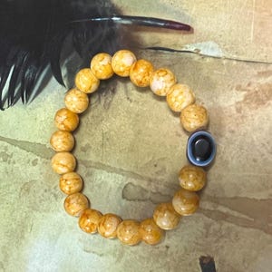 May include: A bracelet made of light brown beads with a blue evil eye charm. The beads have a marbled pattern.