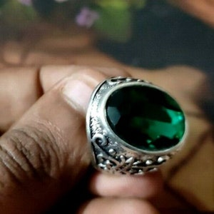 May include: A silver ring with an ornate design and a large, oval-shaped green gemstone.