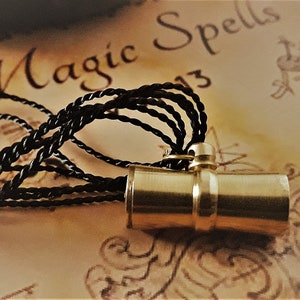 May include: A brass cylinder pendant with a black cord, hanging over a piece of paper with the words "Magic Spells" written in cursive.