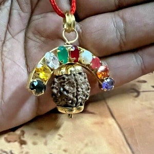May include: A gold pendant with a brown rudraksha bead and a rainbow of gemstones. The pendant is on a red string.