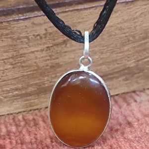 May include: A silver pendant necklace with a brown oval gemstone. The pendant is on a black cord.