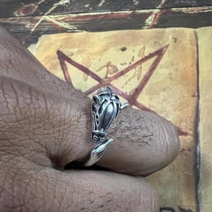 Può includere: Un anello color argento con un design a testa di cavallo. L'anello si avvolge attorno al dito, con la testa di cavallo in alto. L'anello è dettagliato con motivi e trame intricati.
