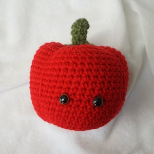 May include: A red crocheted apple with a green stem and black button eyes.