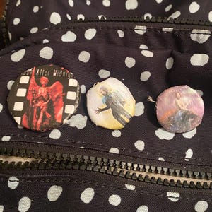 Op de afbeelding: Drie ronde buttons met unieke ontwerpen. Eén button heeft een rood-zwarte afbeelding met de tekst "Moon After Midnight". Een andere heeft een figuur met uitgestrekte armen. De derde button heeft een roze en paarse afbeelding.