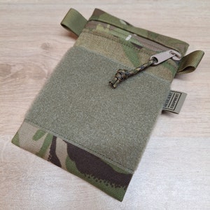 Könnte beinhalten: Eine grüne und braune Camouflage-Tasche mit Reißverschluss und Klettverschluss. Die Tasche hat eine kleine Schlaufe am Reißverschluss und ein Etikett mit der Aufschrift "Resilient Equipment".
