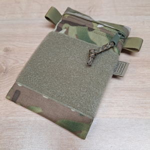 Könnte beinhalten: Eine grüne und braune Camouflage-Tasche mit Reißverschluss und Klettverschluss. Die Tasche hat eine kleine Schlaufe am Reißverschluss und ein Etikett mit der Aufschrift "RESILIENT EQUIPMENT".