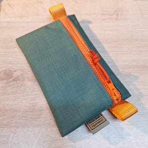 May include: A small, green zippered pouch with an orange zipper and pull tab. The pouch has a small brown label that reads "Resilient Equipment".