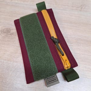 Bolsa EDC simples na cor Borgonha com zíper dourado e painel de alça verde-oliva escuro.