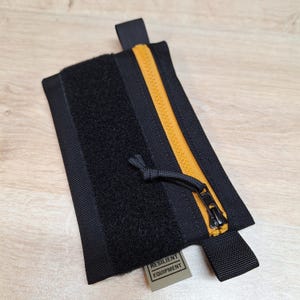 May include: Black zippered pouch with a yellow zipper and a black hook and loop fastener. The pouch has a black strap and a label that reads "RESILIENT EQUIPMENT".