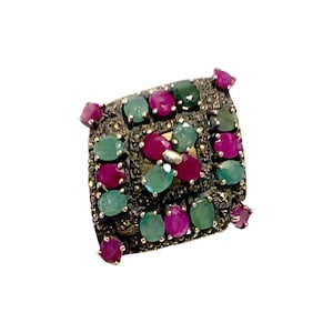 Op de afbeelding: Een zilveren ring met een vierkante zetting met een cluster van groene en roze edelstenen. De ring is versierd met een delicaat patroon van kleine zilveren kralen.