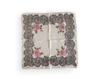 May include: Square, off-white handkerchief with a dark gray lace border. Pink roses with green leaves are printed in each corner. The handkerchief is made of a soft, possibly silk, material.