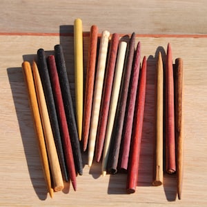 May include: A collection of wooden sticks in various colors, including red, yellow, black, and brown. The sticks are arranged in a fan shape on a wooden surface.