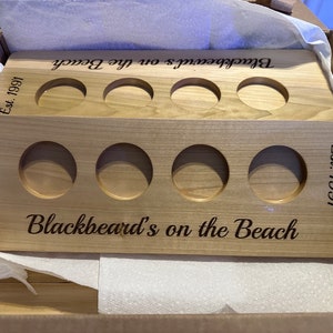 May include: Wooden drink holder with six cup slots. The holder is engraved with "Blackbeard's on the Beach" and "Est. 1991".