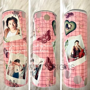May include: A pink tumbler with a grid pattern, featuring photo collages and butterfly illustrations. The tumbler includes images of a person and text that reads "when i run into anything bring me home" and "out of road synchane".