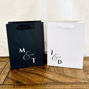 Pu&ograve; includere: Due sacchetti regalo, uno nero e uno bianco, con iniziali eleganti. La borsa nera ha manici in nastro nero e le iniziali "M & T". La borsa bianca ha manici in nastro bianco e le iniziali "J & D".