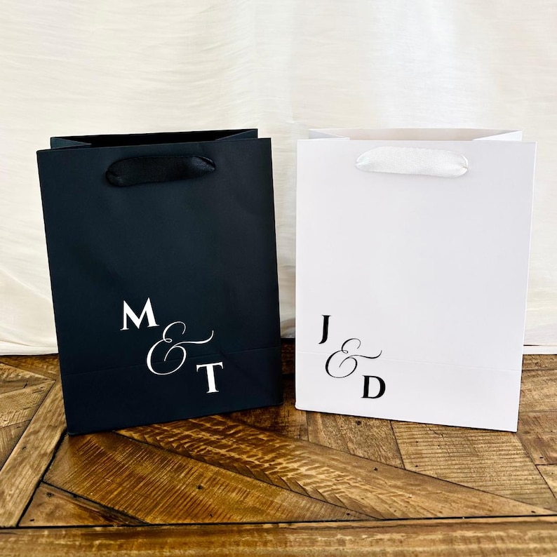 Pu&ograve; includere: Due sacchetti regalo, uno nero e uno bianco, con iniziali eleganti. La borsa nera ha manici in nastro nero e le iniziali "M & T". La borsa bianca ha manici in nastro bianco e le iniziali "J & D".
