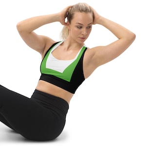 May include: A black, white, and green sports bra. The bra features a white central panel, green side panels, and black trim. The model is wearing black leggings.
