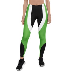 May include: Green, black, and white leggings. The leggings feature a bold design with a green base, black accents on the lower legs, and a white curved stripe down the front. The leggings are form-fitting and suitable for athletic activities.