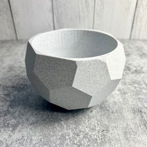 May include: A white geometric planter with a textured surface. The planter is made of a durable material and has a unique, modern design.