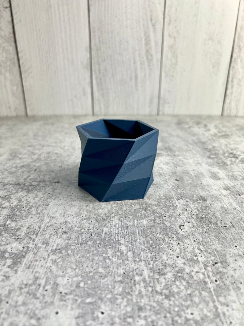 May include: A dark blue geometric planter with a hexagonal shape. The planter is made of a smooth, textured material.