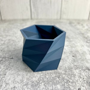 May include: A dark blue geometric planter with a hexagonal shape. The planter has a textured surface and is made of a durable material.