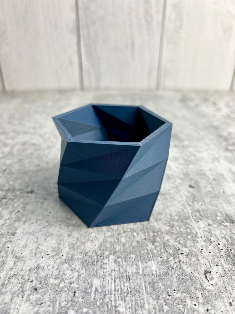 May include: A dark blue geometric planter with a hexagonal shape. The planter has a textured surface and is made of a durable material.