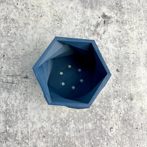 May include: A dark blue hexagonal planter with drainage holes. The planter is made of a smooth, textured material.