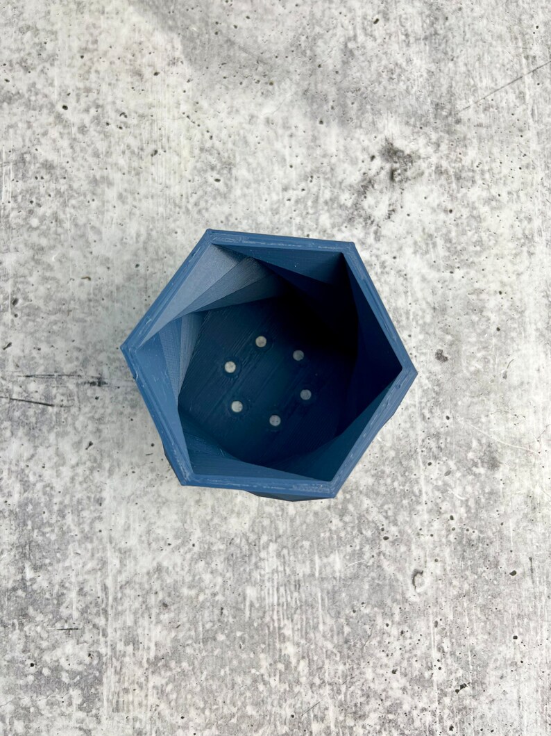 May include: A dark blue hexagonal planter with drainage holes. The planter is made of a smooth, textured material.