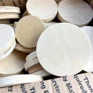 May include: A box filled with round, unfinished wooden circles of various sizes. The circles are made of light-colored wood and have a smooth surface.