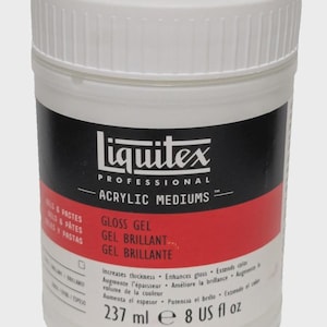 May include: A white plastic jar of Liquitex Professional Acrylic Mediums Gloss Gel. The label features black and red bands with white text, including the product name, volume of 237 ml and 8 US fl oz, and descriptions in English, French, and Spanish.