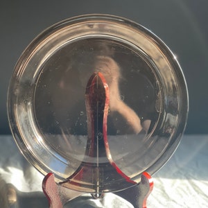 May include: A clear glass pie plate with a slightly rippled surface, resting on a dark brown wooden stand.