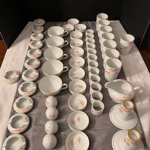May include: A set of white porcelain dishes with a delicate floral design in shades of pink and brown. The set includes cups, saucers, bowls, and other serving pieces.