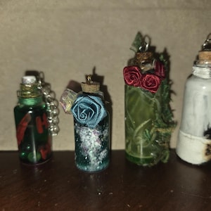 May include: Four decorative glass bottles with cork stoppers. One bottle has the word "H" in red paint. Another has a blue rose, and another has red roses. The last bottle is painted black and white.