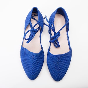 May include: A pair of blue woven flat shoes with laces. The shoes have a pointed toe and are made of a woven material.