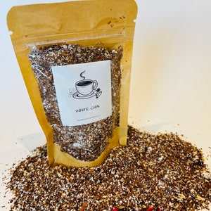 Puede incluir: Una bolsa transparente llena de mezcla de té chai blanco, con un respaldo de papel kraft. La etiqueta presenta una ilustración de una taza de café y las palabras "WHITE CHAI". La mezcla de té está esparcida alrededor de la bolsa.