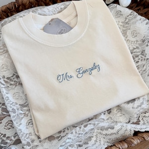 May include: A white ceramic mug with a black handle and the text "But First, Coffee" in a black, handwritten-style font. The mug is on a white surface.