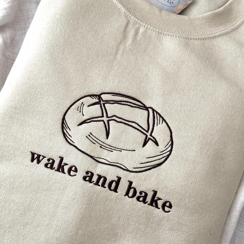 May include: A beige sweatshirt with a brown embroidered image of a loaf of bread and the text "wake and bake".