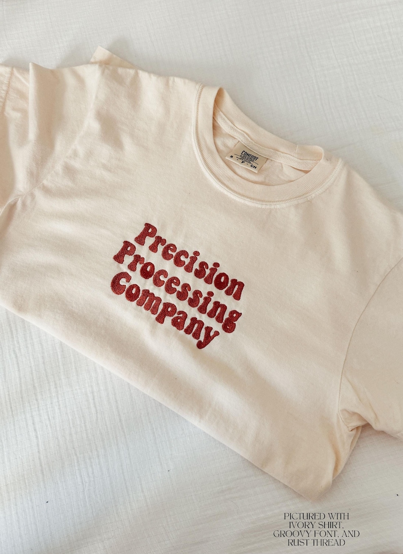 Puede incluir: Camiseta de color marfil con la frase "Precision Processing Company" en una fuente retro color &oacute;xido. La camiseta es de un material suave y tiene un dise&ntilde;o cl&aacute;sico de cuello redondo. Una etiqueta es visible en el cuello.