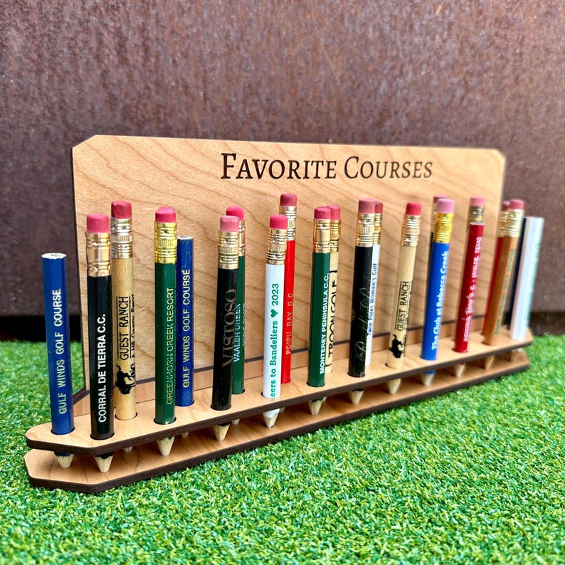 May include: A wooden stand with the words "FAVORITE COURSES" engraved on it. The stand holds 18 pencils, each with a different golf course logo printed on it.