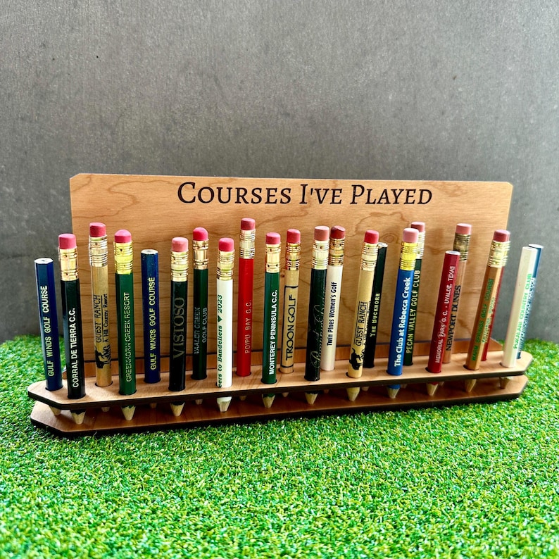 May include: A wooden stand with the text "COURSES I'VE PLAYED" engraved on it. The stand holds 20 golf pencil toppers with different golf course names printed on them.