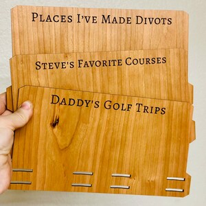May include: Three wooden plaques with engraved text. The top plaque reads "Places I've Made Divots". The middle plaque reads "Steve's Favorite Courses". The bottom plaque reads "Daddy's Golf Trips".