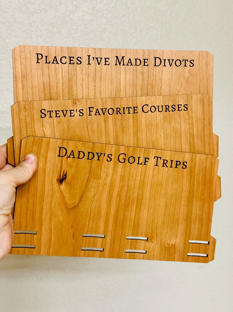 May include: Three wooden plaques with engraved text. The top plaque reads "Places I've Made Divots". The middle plaque reads "Steve's Favorite Courses". The bottom plaque reads "Daddy's Golf Trips".