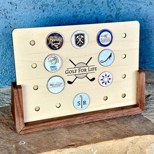 May include: A wooden golf ball display stand with a walnut base. The stand has 10 holes for displaying golf balls. The stand has the text "GOLF FOR LIFE" printed on it.