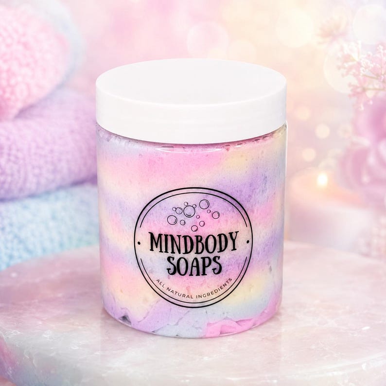 May include: A clear plastic jar filled with pastel-colored whipped soap in swirls of pink, yellow, and blue. The jar has a white screw-top lid and a circular black label featuring the text MINDBODY SOAPS and ALL NATURAL INGREDIENTS.