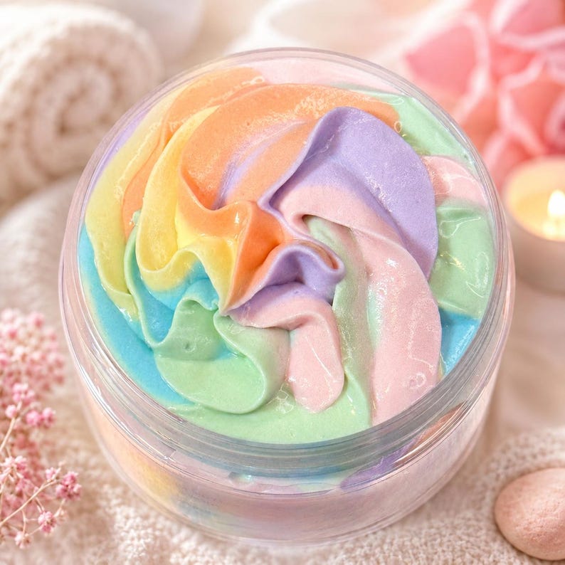 May include: A clear plastic jar filled with whipped body butter featuring a swirled, multi-colored design. The cream displays vibrant shades of pastel orange, yellow, light blue, soft green, lavender, and pale pink, arranged in a decorative spiral.