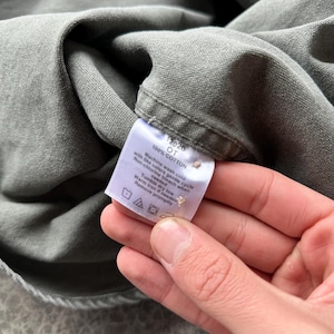 May include: A white ceramic mug with a black handle and the text "But First, Coffee" in a handwritten style. The mug is on a white surface. The mug is approximately 4 inches tall.